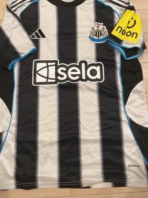 Newcastle United matchtröja Adidas S - Snygg Newcastle United matchtröja från Adidas i svart och vitt med blå detaljer. Tröjan har klubbmärke, sponsorloggor och är tillverkad i lätt funktionsmaterial (AEROREADY) med slim fit-passform. Perfekt för fotbollsträning eller att bära på läktaren.