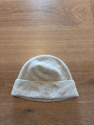 Ljusgrå mössa från Sandö - Snygg ljusgrå mössa från Sandö i mjukt stickat material. Klassisk modell med uppvikt kant och enkel design som passar till det mesta. Perfekt för kyliga dagar när du vill hålla stilen enkel och clean.