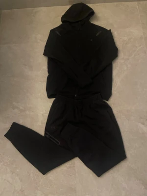 Svart träningsset från Under Armour  - Säljer en tracksuit från Under Armour med resår i midjan och muddar vid bensluten. Byxorna har en dragkedjeförsedd ficka på sidan och är tillverkade i mjukt material som passar perfekt för träning eller chill. Storlek: M, funkar även för S också skulle jag säga. Skicket är mycket bra. Pris går att diskutera😊