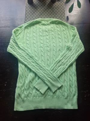 Ljusgrön kabelstickad tröja Morris gents - Snygg ljusgrön kabelstickad tröja från Morris gents med rund halsringning och diskret logga broderad på bröstet. Tröjan har långa ärmar och ribbade muddar vid ärmslut och nederkant. Perfekt för en stilren och fräsch look.