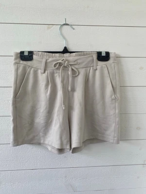 Mjuka beiga shorts. - Snygga beige shorts med elastisk midja och snörning framtill. Shortsen har fickor på sidorna och dekorativa bakfickor. Perfekta för varma dagar och enkel att matcha med olika toppar.