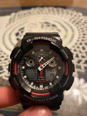Svart Casio G-Shock digital klocka - Tuff svart G-Shock klocka från Casio med digital och analog display. Klockan har robust design, röda detaljer och flera funktioner som datum, veckodag och stoppur. Perfekt för dig som gillar sportig och tålig stil.