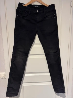 Svarta Replay Anbass - Snygga svarta slim fit jeans från Replay med klassisk femficksmodell och diskreta detaljer. Jeansen har normal midja och är tillverkade i ett stretchigt material för skön passform. Perfekta för dig som gillar en stilren och modern look.