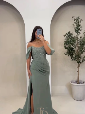 Klänning fest/bal - Elegant grön långklänning med offshoulder-ärmar och vacker pärldekor upptill. Klänningen har en figurnära passform, draperade detaljer i midjan och en hög slits framtill. Perfekt för speciella tillfällen. Meddela gärna för frågor har fler bilder att se. Säljer endast via meddelanden