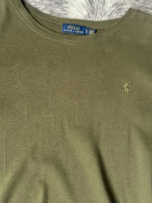 Olivgrön t-shirt från Polo Ralph Lauren - Olivgrön t-shirt från Polo Ralph Lauren med klassisk rund halsringning och broderad logga på bröstet. Tillverkad i mjuk bomull för en skön känsla. Perfekt för en avslappnad och stilren look.