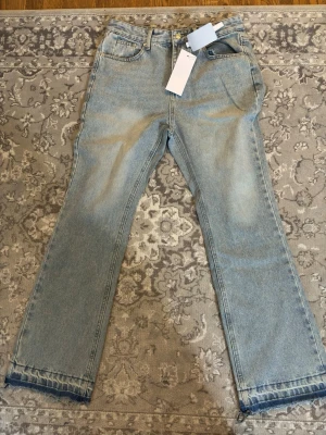 Ljusblå raka jeans med rå kant - Ljusblå jeans med rak passform och rå, fransad kant nertill. Klassisk femficksmodell med bälteshällor och dragkedjegylf. Jeansen har en avslappnad vibe och är perfekta för en trendig streetstyle-look.
