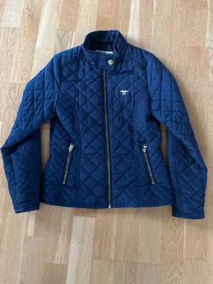 Marinblå quiltad jacka Hampton Republic - Snygg marinblå quiltad jacka från Hampton Republic med ståkrage och dragkedja framtill. Jackan har två fickor med dragkedja och ett diskret logomärke på bröstet. Perfekt för dig som gillar klassisk och sportig stil.