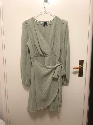 Ljusgrön omlottklänning med knyt - Söt ljusgrön omlottklänning från H&M med små vita prickar. Klänningen har lång ärm, v-ringning och knyt i midjan. Den är kort i modellen och har en lätt volangkant nertill. Perfekt för vår och sommar!