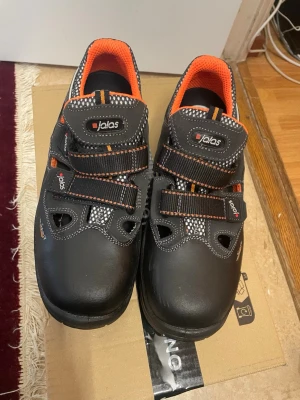 Svarta Jalas Arbetsskor - Säljer Jalas 3400A Monza Sport skyddssandaler S1. Passar i arbetsmiljöer där det finns behov av grundläggande säkerhet. Kardborreknäppningen gör det enkelt att ta på och av.   Skorna har använts inom en kort period, och aldrig mer. Ser ut som nya. Säljs för ca 1500 kr online.   För mer info om skornas fantastiska egenskaper, sök på modellen online, eller tveka inte att höra av dig!