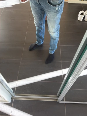 Ljusblå slitna jeans med raka ben - Säljer ett par ljusblå jeans med raka ben och slitningar på både fram- och baksida. Jeansen har klassisk femficksdesign och är tillverkade i denim. Perfekta för en avslappnad och trendig look. Modellen är 185 och 70 kilo  31/32 i storlek 