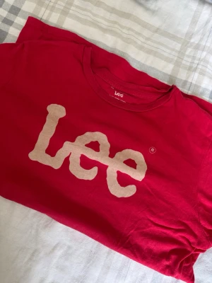 Röd Lee t-shirt med stor logga - Säljer en röd t-shirt från Lee med stor vit logga framtill. Klassisk rund hals och korta ärmar. Tillverkad i mjuk bomull som är skön att bära. Perfekt för dig som gillar streetwear och vill ha en enkel men snygg look.