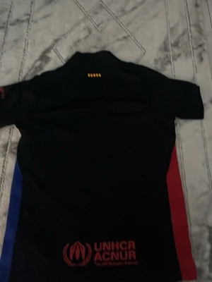 Svart FC Barcelona matchtröja Nike - Säljer en svart FC Barcelona matchtröja från Nike med röda och blå detaljer på sidorna. Tröjan har klubbmärke, Nike-logga och Spotify-logga på bröstet samt UNHCR-tryck på ryggen. Perfekt för fotbollsträning eller att bära som supporter.