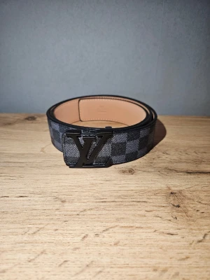 Rutigt svart bälte  - Snyggt svart rutigt bälte.Insidan är beige och bältet har en stilren look som passar till jeans eller kostymbyxor. Perfekt accessoar för att lyfta din outfit.
