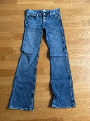 Blåa bootcut jeans med tre knappar - Jättefina blåa bootcut jeans med tre knappar vilket är super snyggt! De är lågmidjade och från gina tricot young! Storleken är 146 tall, innerbenslängd är 77cm!