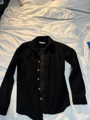 Svart manchester overshirt från Erla  - Stilren svart overshirt i manchestertyg . Perfekt till sena sommarkvällar 