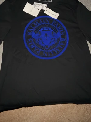Svart t-shirt från Balmain Paris - Helt ny och oanvänd Balmain T-shirt med originaltags kvar. Köpt från MR PORTER. Nypris var 281 € (ca 3 150 kr).  Tyvärr tappades kvittot bort, vilket gjorde att den inte kunde returneras. Därför säljs den nu till ett betydligt lägre pris, ett bra tillfälle att köpa en äkta Balmain tröja till ett riktigt bra pris.  Skicka gärna ett meddelande vid frågor eller intresse!
