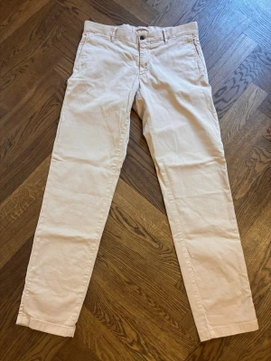 Beige chinos med raka ben - Jlindeberg - Snygga beige chinos med raka ben och klassisk passform. Byxorna har bälteshällor, knappgylf och två bakfickor med knapp. Tillverkade i ett mjukt bomullstyg som ger en clean och stilren look.