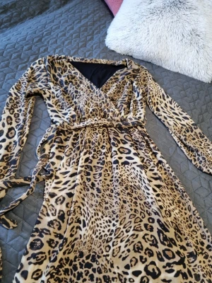 Leopardmönstrad klänning med bälte - Säljer en leopardmönstrad omlottklänning i beige och svart med lång ärm och v-ringning. Klänningen har ett matchande bälte i midjan och är i mjukt, följsamt material.Jag är inte säker på storleken, men den kan passa någon som har storlek 38/40. Använd en gång. 