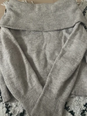 Ljusgrå stickad polotröja H&M - Mysig ljusgrå stickad polotröja från H&M med bred ribbad krage och muddar. Tröjan har lång ärm och är tillverkad i mjukt material som passar perfekt för kyligare dagar. Enkel och stilren design som är lätt att matcha.