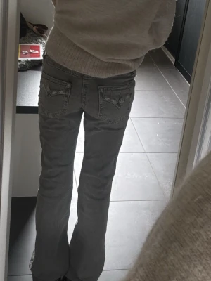 Grå bootcut jeans med broderade fickor - Säljer ett par grå bootcut jeans med låg/medel midja och snygga broderade detaljer på bakfickorna❤️