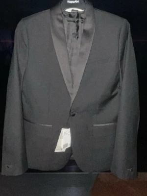 Svart kostym från H&M - Snygg svart kostym från H&M med klassisk kavaj och matchande byxor. Kavajen har slimmad passform, satinkrage och knappar vid ärmslut. Perfekt för dig som vill ha en stilren och tidlös look.