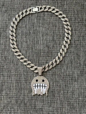 Iced out halsband med smiley-hänge - Snyggt halsband i silverfärg med grov kedja och ett stort smiley-hänge täckt av glittrande stenar. Hänget har svarta ögon och ett vitt, droppande leende med svarta detaljer. Perfekt för dig som gillar statement-smycken och streetstyle. (Barn storlek)