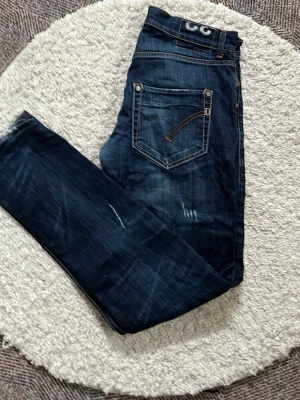 Dondup mörkblå slim fit jeans med slitningar - Snygga mörkblå jeans i slim fit-modell med slitna detaljer och kontrastsömmar. Jeansen har klassiska fem fickor och en cool tvättad look. Perfekta för dig som gillar en avslappnad men trendig stil.