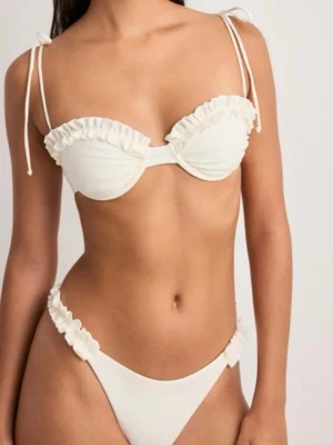 Vit bikini med volang och knyt - Supersöt vit bikini med volangdetaljer på både överdel och underdel. Överdelen har bygel och smala axelband med knyt. BH i 70A och underdel i XS. Säljer båda två tillsammans för 179kr. 