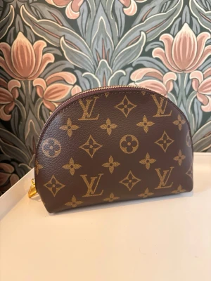 Brun sminkväska el necessär fint mönster trendig och klassisk - Snygg brun sminkväska el necessär i klassiskt monogrammönster med guldfärgad dragkedja. Halvmåneformad design perfekt för att hålla ordning på smink och småsaker. En ikonisk accessoar för dig som gillar lyxig stil.