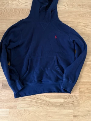 Mörkblå hoodie från Polo Ralph Lauren - Mörkblå hoodie från Polo Ralph Lauren med klassisk huva och känguruficka. Liten röd broderad logga på bröstet. Tillverkad i mjukt bomullsmaterial som är skönt att bära. Perfekt för en avslappnad och stilren look. Priset ej hugget i sten. Hör av vid funderingar