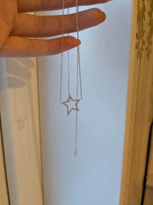 Silverhalsband med stjärnhänge - Snyggt halsband i silverfärgad metall med ett öppet stjärnformat hänge. Kedjan är tunn och elegant, och stjärnan har en minimalistisk design. Perfekt för dig som gillar stilrena accessoarer med en twist.köpt i Kina 