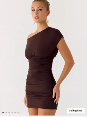 Peppermayo klänning ny - Säljer en brun, tight kortklänning med oneshoulder-design och rynkade detaljer längs sidorna. Klänningen har en smickrande passform och är tillverkad i ett stretchigt syntetmaterial som sitter snyggt på kroppen. Den är från peppermayo, säljer åt min tjej då den inte satt bra på henne 