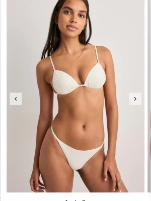 Vit bikini med smala band - Stilren vit bikini med smala axelband och trekantsformad topp. Underdelen har en klassisk, enkel design med hög skärning. Perfekt för strandhäng eller poolen. Materialet känns mjukt och följsamt mot huden.