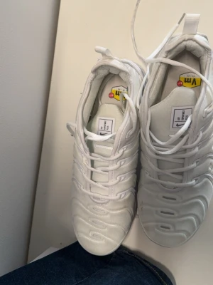 Vita Nike Air Vapormax Plus sneakers - Säljer ett par fräscha vita Nike Air Vapormax Plus sneakers med ikonisk bubbelsula och snyggt mönstrad ovandel. Skorna har snörning och tydliga Nike-detaljer. Perfekta för dig som vill ha en clean och modern look.