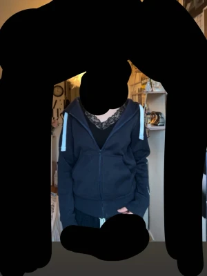 Mörkblå zip hoodie med vita snören - Mörkblå hoodie med dragkedja framtill och vita dragsnören i huvan. Klassisk känguruficka och ribbade muddar vid ärmslut och nederkant. Perfekt för en avslappnad och chill stil. Materialet ser ut att vara mjuk bomullsblandning.