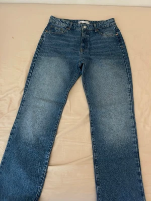 Blå raka jeans från Zara - Säljer ett par klassiska blå raka jeans från Zara. Jeansen har hög midja, fem fickor och en snygg tvättad look. Materialet är kraftig denim i bomull och passformen är relaxed med raka ben. Perfekta till en avslappnad stil.