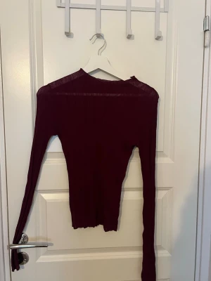 Vinröd tunn långärmad tröja - Säljer en vinröd, tunn och figurnära långärmad tröja med rund hals. Perfekt att styla lager på lager eller bära som den är. Enkel och stilren design utan synliga detaljer eller mönster.
