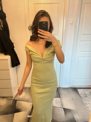 Ljusgrön lång axelbandslös klänning - Snygg ljusgrön långklänning med offshoulder-design och djup v-ringning. Klänningen har en figurnära passform och är tillverkad i ett slätt material som ger en elegant siluett. Perfekt för dig som vill sticka ut med en stilren look.