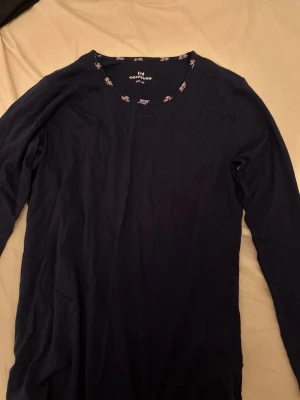 Mörkblå långärmad pyjamas topp - En enkel och stilren mörkblå långärmad topp med rund halsringning. Tillverkad i mjuk bomull, perfekt som pyjamas tröja. Halsringningen har en liten detalj med tryckt text och mönster.