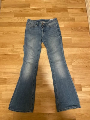 Blå bootcut jeans med utsvängda ben - Säljer ett par ljusblå bootcut jeans med klassisk femficksmodell och utsvängda ben. Jeansen har en snygg tvätt med slitningar på låren och knäna. Perfekta för en avslappnad och trendig look. Lite smuts  fläckar vid foten längst ner 