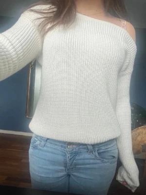 Off shoulder stickad tröja vit - Trendig off shoulder stickad tröja i vit med ribbad struktur. Långa ärmar och avslappnad passform, perfekt att styla med jeans. Mjuk och skön, passar dig som gillar en enkel men snygg look.