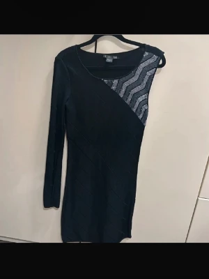 Svart oneshoulder klänning med glitter från Armani  - Snygg svart oneshoulder klänning med lång ärm och glittrig detalj i silver på ena axeln. Klänningen är kort och har en tight passform, perfekt för dig som vill sticka ut. Materialet känns stretchigt och bekvämt. Priset går även att diskuteras då det finns en defekt på klänning! OBS: FRAKTAR INOM 24H!🩷
