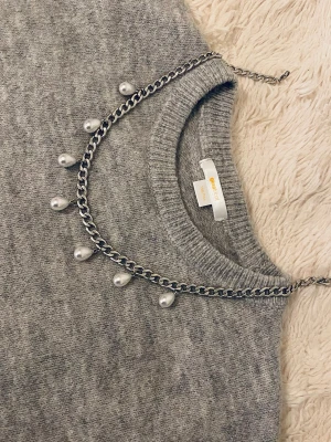 Silverfärgat halsband med pärldroppar - Snyggt halsband i silverfärgad metallkedja med sju droppformade vita pärlor som hänger längs kedjan. Kedjan har en modern, chunky look och pärlorna ger en elegant touch. Perfekt accessoar för att lyfta din outfit.