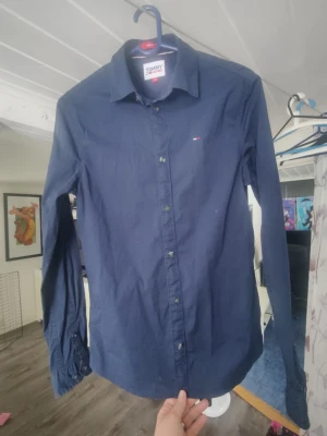 Mörkblå skjorta från Tommy Hilfiger - Klassisk mörkblå skjorta från Tommy Hilfiger med diskret logga på bröstet. Skjortan har lång ärm, knappar framtill och en stilren krage. Perfekt till jeans eller chinos för en clean look.