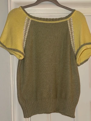 Grön och gul stickad topp - Säljer en unik stickad topp med olivgrön kropp och ljusgula, korta ärmar, samt dekorativa stickade detaljer längs ärmsömmarna. 