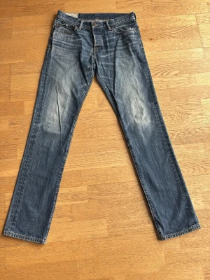 Abercrombie & Fitch Jeans - Säljer ett par klassiska blå jeans med raka ben. Jeansen har fem fickor, knappgylf och tydliga kontrastsömmar. Jeansen har storleken W30 L32. Hör av dig vid frågor!
