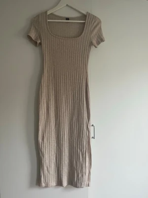Beige ribbad midiklänning - Beige ribbad klänning med korta ärmar och fyrkantig ringning. Klänningen är figurnära och har en mjuk, stretchig känsla. 
