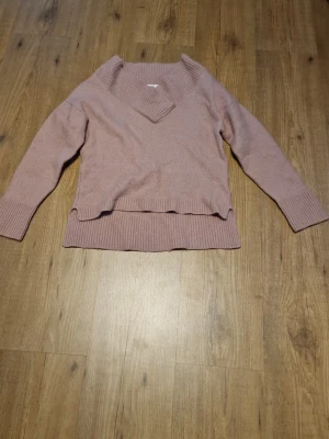 Rosa stickad tröja - Mysig stickad tröja i ljusrosa med bred v-ringad krage och ribbade muddar vid ärmslut och nederkant. Tröjan har en avslappnad passform och är perfekt för lager på lager. Materialet känns mjukt och behagligt mot huden.