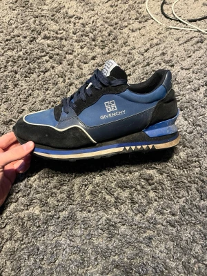 Blå sneakers från Givenchy - Snygga blå sneakers från Givenchy med vita och svarta detaljer. Skon har en låg siluett, svart sula med mönster och Givenchy-logga på sidan och plösen. Materialmix av mocka och textil för en modern look. Utan box