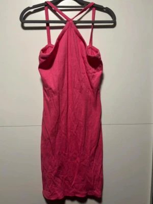 Rosa kort klänning med smala band - Snygg rosa kort klänning med smala axelband som korsas i ryggen. Klänningen har en enkel och rak passform, perfekt för varma dagar. Tillverkad i mjukt material som känns bekvämt mot huden.